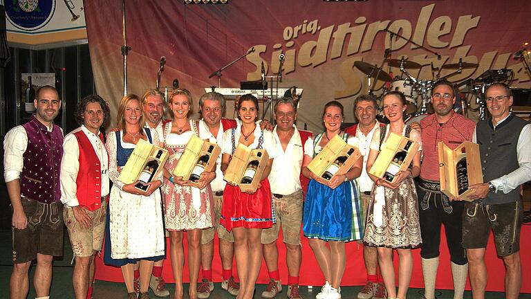 Gastgeschenke beim 30. Südtiroler Weinfest in Esselbach: Spielmannszugvorsitzender Manuel Heim (links), zweiter von rechts Kellereiobmann Andreas Kofler, rechts: Stellvertretender Vorsitzender Uli Heim. Dazwischen die „Südtiroler Spitzbuam“ und die Mädchen, die ihnen die Magnumflaschen überreichten. Gastgeschenke beim 30. Südtiroler Weinfest in Esselbach: Spielmannszugvorsitzender Manuel Heim (links), zweiter von rechts Kellereiobmann Andreas Kofler, rechts: Stellvertretender Vorsitzender Uli Heim. Dazwischen die „Südtiroler Spitzbuam“ und die Mädchen, die ihnen die Magnumflaschen überreichten.