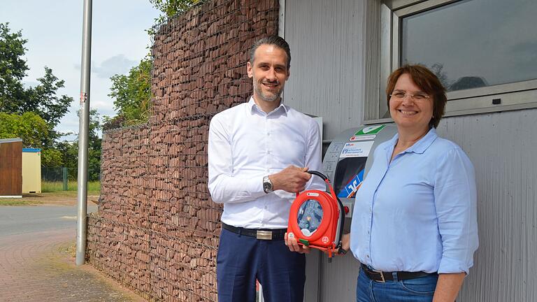 Tomas Virsik von der Raiffeisenbank Main-Spessart und Inge Albert vom Stadtmarketing freuen sich über den neuen Defibrillator am Festplatz Martinswiese in Marktheidenfeld.