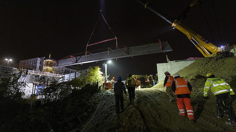 Ein Kran hebt an der Baustelle zur neuen Siligmüllerbrücke in Würzburg einen der drei riesigen Stahlträger in die Verankerungen beidseits der Bahnlinie.