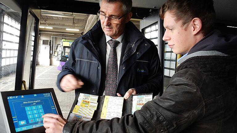 Harald Mendrock zeigt den alten &bdquo;Bauchladen&ldquo;, Christoph Jaskula, Auszubildender im Fahrbetrieb, den Bildschirm des Bordcomputers, der dem Fahrer auch anzeigt, ob das eTicket des Fahrgasts gültig ist.