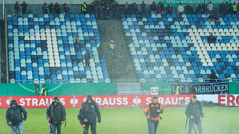 1. FC Saarbrücken - Bor. Mönchengladbach       -  Im Ludwigspark-Stadion versuchen Helfer, Wasserlachen vom Spielfeld zu entfernen.