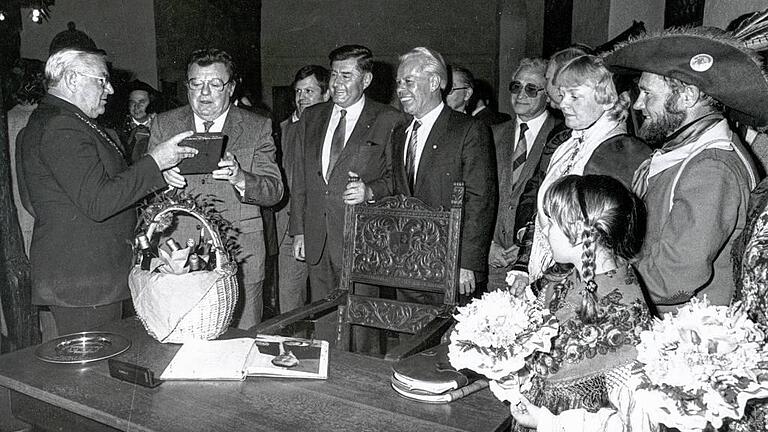 Der Ehrengast: Dieses Bild entstand am 7. Mai 1982 in Karlstadt. FJS erhält vom damaligen Bürgermeister Werner Hofmann einen Präsentkorb und ein Buch über die Stadt. Zuvor hatte Strauß sich ins Goldene Buch eingetragen. Neben lokaler Politprominenz mit auf dem Bild die Symbolfiguren Spessarträuber und Winzerin.