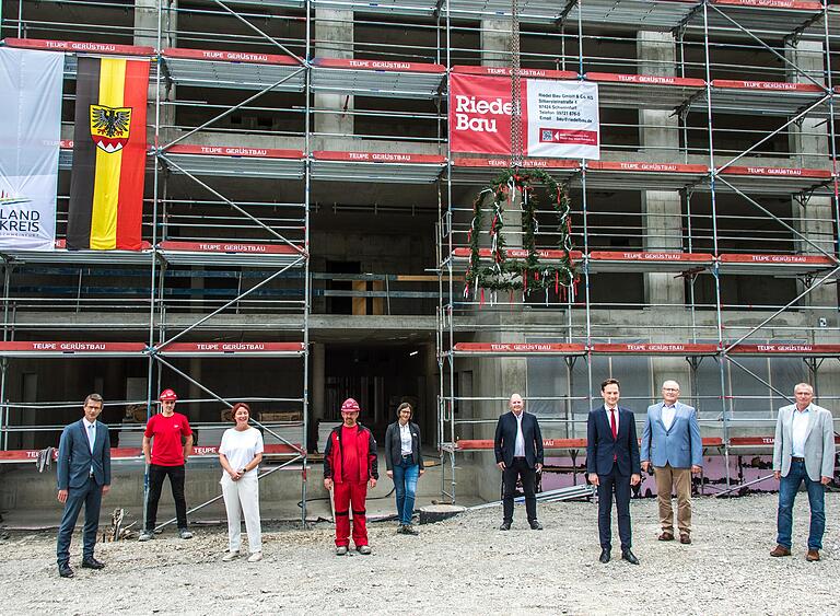 Richtfest-Gruppenbild mit Abstand am entstehenden Berufsschulzentrum Alfons Goppel. Neben OB Sebastian Remelé (links), Vertretern der Firma Riedel Bau (Aufsichtsratsvorsitzende Stefanie Riedel, Dritte von links) und Architekt Peter Schwinde (Vierter von rechts),freuten sich auch Landrat Florian Töpper (Zweiter von rechts) und Schulleiter Joachim Sagstetter (rechts) über den Baufortschritt.