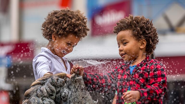 Emdlich wieder Sommer       -  Nach Wochen mit viel Regen und fast herbstlichen Temperaturen ist seit wenigen Tagen der Sommer zurück. Bei schwülen Temperaturen um die 27 Grad zieht es am Sonntag (13.08.23) einige Menschen nach draußen. Kinder spielen an einem Brunnen am Sternplatz in Würzburg.