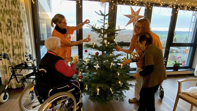 Rote und goldene Kugeln uns Strohsterne: Diesen Christbaumschmuck haben sich die Bewohnerinnen und Bewohner einer Hausgemeinschaft im Franziska-Streitel-Altenheim ausgesucht. Gemeinsam mit den Pflegerinnen schmücken sie den Baum.
