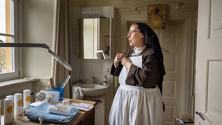 Schwester Clara-Maria bekleidet sich in der Kerzenwerkstatt mit einer Arbeitsschürze im Kloster Rödelmaier.