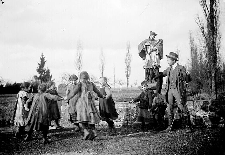 Zu sehen sind Kinder der Grundschule Goßmannsdorf mit dem 1924/1925 in Goßmannsdorf tätigen Aushilfslehrer Wilhelm Huhn, der sich hier als Fotograf ausgibt. Aufgenommen wurde die Szene&nbsp; vermutlich in Röttingen an der damals noch nicht verrohrten Rippach.