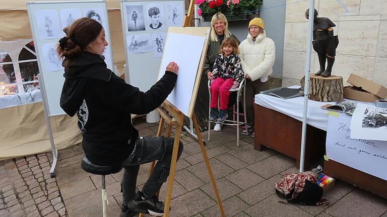 Genuss- und Kunsthandwerkermarkt in Bischofsheim lockte trotz kühler Temperaturen viele Besucher an.
Eine Schülerin der Holzschnitzsschule zeichnete Porträts. Genuss- und Kunsthandwerkermarkt in Bischofsheim lockte trotz kühler Temperaturen viele Besucher an.
Eine Schülerin der Holzschnitzsschule zeichnete Porträts.