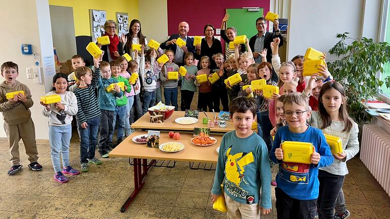 Die Erstklässlerinnen und Erstklässler der Grundschule in Wollbach vor dem bio-regionalen Frühstücksbüfett. Mit ihnen freuen sich Landrat Thomas Habermann (hinten Mitte), Bürgermeister Thomas Bruckmüller (hinten rechts), Svenja Arbes, Projektmanagerin der Öko-Modellregion Rhön-Grabfeld (hinten, zweite von rechts) sowie Sabina Urban, Rektorin der Grundschule Hollstadt-Wollbach (hinten links) und die Lehrerinnen der ersten Klassen.