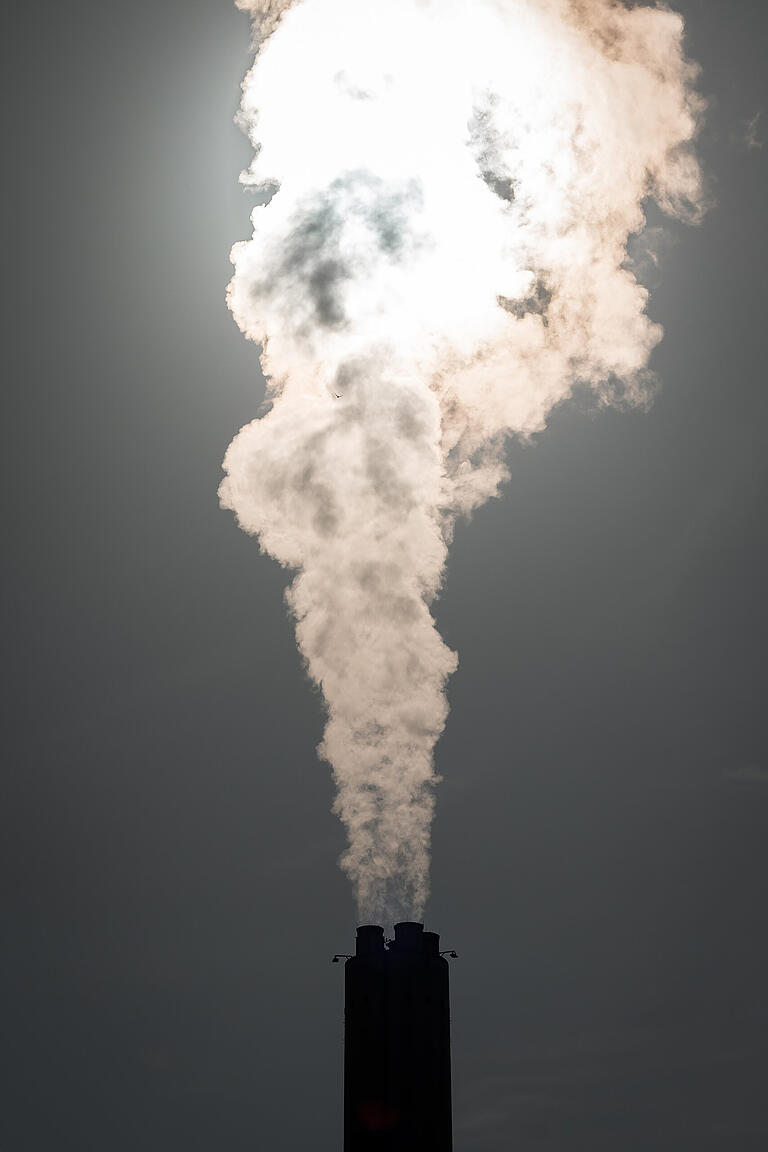 Der Schlot eines Industriekomplexes nahe Schweinfurt stößt früh am Morgen heiße Luft in den Himmel.