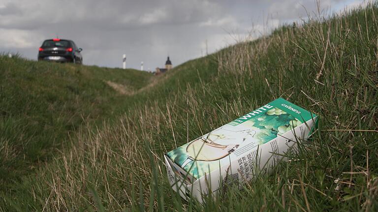 Einer von vielen: Ein Weißwein-Tetra-Pak liegt in einem Straßengraben an der Kreisstraße zwischen Herlheim (im Bild der Herlheimer Kirchturm) und Zeilitzheim.