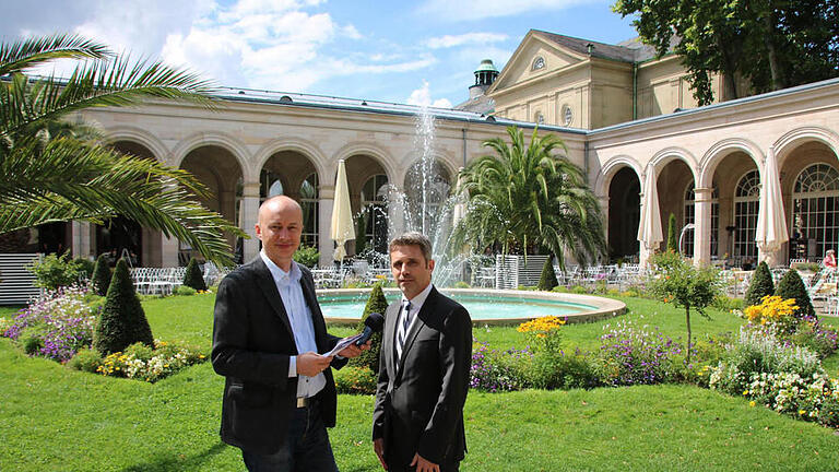 Interview-Termin in malerischer Atmosphäre: Redakteur Ralf Ruppert (von links) traf sich mit Kurdirektor Frank Oette im Kurgarten, im Hintergrund ein Teil des Arkedenbaus und der Regentenbau. Foto: Sebastian Elsässer       -  Interview-Termin in malerischer Atmosphäre: Redakteur Ralf Ruppert (von links) traf sich mit Kurdirektor Frank Oette im Kurgarten, im Hintergrund ein Teil des Arkedenbaus und der Regentenbau. Foto: Sebastian Elsässer