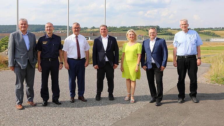 Gruppenfoto mit Autobahn im Rücken mit (von links) Wolfgang Wüst (Abteilungsleiter Straßen- und Brückenbau im bayerischen Verkehrsministerium), Harald Hoffmann (Leitender Polizeidirektor Polizeipräsidium Unterfranken), Bürgermeister Ernst Nickel, Verkehrs- und Bauminister Christian Bernreiter, Landrätin Tamara Bischof, Reinhard Pirner (Direktor der Autobahn GmbH des Bundes, Niederlassung Nordbayern) und Stephan Ried (Projektleiter ÖPP Autobahn GmbH des Bundes).&nbsp;