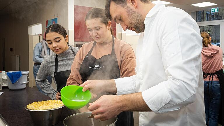 Maximilian Morhard vom Hotel und Gasthof Bären in Randersacker hilft Schülerinnen bei der Zubereitung des Nachtisches.&nbsp;