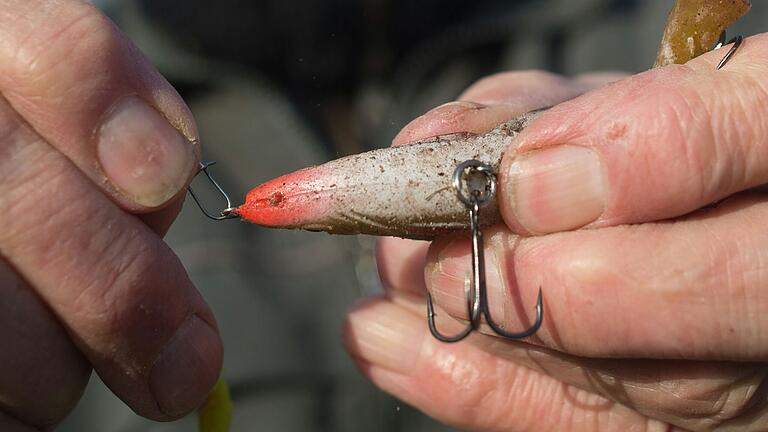 Ein Angler bereitet seine Angel vor und hängt einen Drilling an die Angelschnur. (Symbolbild)