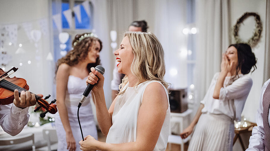 A young woman singing on a wedding reception, bride and guests dancing.       -  A young woman singing on a wedding reception, bride and guests dancing in the background.