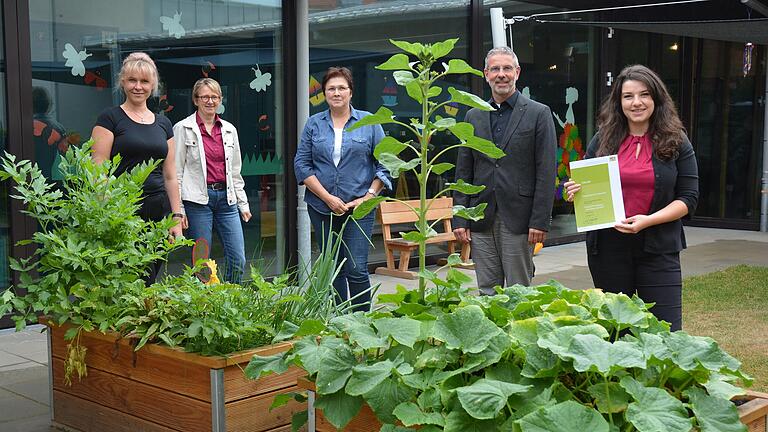 Gesundes aus dem Hochbeet für die Küche der Kita. Über die Auszeichnung freuen sich (von links) Küchenleiterin Marina Prinz, Beate Laumeyer von der Vernetzungsstelle Kita- und Schulverpflegung Unterfranken, Kita-Verpflegungsbeauftragte Brigitte Rossbach, Dekan Dr. Matthias Büttner und Kita-Leiterin Giulia Castro Diaz mit der Urkunde.