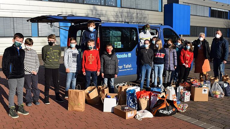 Das Foto zeigt einen ehrenamtlichen Helfer und eine Mitarbeiterin der Lohrer Tafel zusammen mit Kindern der fünften Klasse beim Einladen der Spendentüten in das Lohrer Tafel-Mobil.