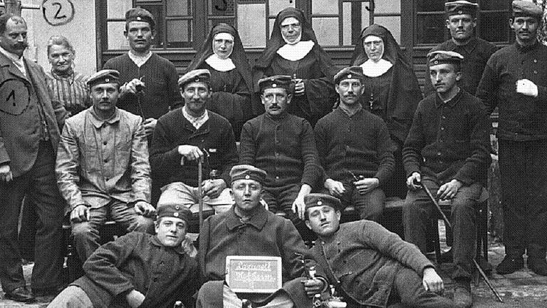 Verwundete im Hof des alten Kindergartens im Jahr 1915: Diese Aufnahme entstand während des 1. Weltkrieges im Hof des städtischen Kindergartens, in dem ein Lazarett für Verwundete errichtet worden war. Hintere Reihe von links: Michael Geyer, Köchin Peppi Bersenfelder, die Ordensschwester Anette, Oberin Sigfrieda Schneider und Handarbeitsschwester Flora. Verwundete im Hof des alten Kindergartens im Jahr 1915: Diese Aufnahme entstand während des 1. Weltkrieges im Hof des städtischen Kindergartens, in dem ein Lazarett für Verwundete errichtet worden war. Hintere Reihe von links: Michael Geyer, Köchin Peppi Bersenfelder, die Ordensschwester Anette, Oberin Sigfrieda Schneider und Handarbeitsschwester Flora.