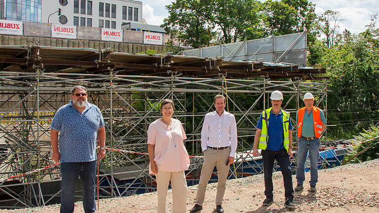 Unter dem Schutzgerüst rauschen die Züge durch die Baustelle. Im Hintergrund ist die Betonpfahlwand zu sehen, die an der Waltherstraße die Baustelle vom Stadtring abstützt. Von links: : Georg Maier, (Ingenieurbüro Maier), Annette Messerer (Leiterin des Fachbereichs Tiefbau und Verkehrswesen), Baureferent Benjamin Schneider, Leonhard Gehrig und Michael Göcke (beide Brücken- und Ingenieurbau Fachbereich Tiefbau und Verkehrswesen). Unter dem Schutzgerüst rauschen die Züge durch die Baustelle. Im Hintergrund ist die Betonpfahlwand zu sehen, die an der Waltherstraße die Baustelle vom Stadtring abstützt. Von links: : Georg Maier, (Ingenieurbüro Maier), Annette Messerer (Leiterin des Fachbereichs Tiefbau und Verkehrswesen), Baureferent Benjamin Schneider, Leonhard Gehrig und Michael Göcke (beide Brücken- und Ingenieurbau Fachbereich Tiefbau und Verkehrswesen).