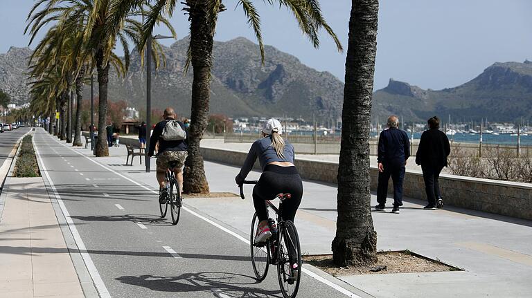 Menschen fahren am Hafen von Pollença auf Mallorca mit dem Fahrrad. Die spanische Insel ist von Touristen wirtschaftlich abhängig. Daher wünschen sich viele Mallorquiner, darunter die Ärztin Dr. Ute Schreiner, dass viele Urlauber die Insel alsbald wieder besuchen. Menschen fahren am Hafen von Pollença auf Mallorca mit dem Fahrrad. Die spanische Insel ist von Touristen wirtschaftlich abhängig. Daher wünschen sich viele Mallorquiner, darunter die Ärztin Dr. Ute Schreiner, dass viele Urlauber die Insel alsbald wieder besuchen. 