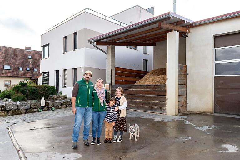Michael und Sabine Bürger zusammen mit ihren Kindern Fritz und Vroni und Hund 'Piesel' auf ihrem Anwesen in der Schafgasse in Unterspiesheim. Im Hintergrund ist ein Hackschnitzellager zu sehen.