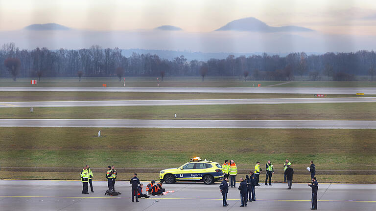 Klimaaktivisten angeklebt auf Rollfeld am Münchner       -  08.12.2022, Bayern, München: Vier Klimaaktivisten sitzen mit angeklebten Händen auf dem Zubringer einer Start-und Landebahn am Airport Franz-Josef-Strauß. Foto: Karl-Josef Hildenbrand/dpa +++ dpa-Bildfunk +++