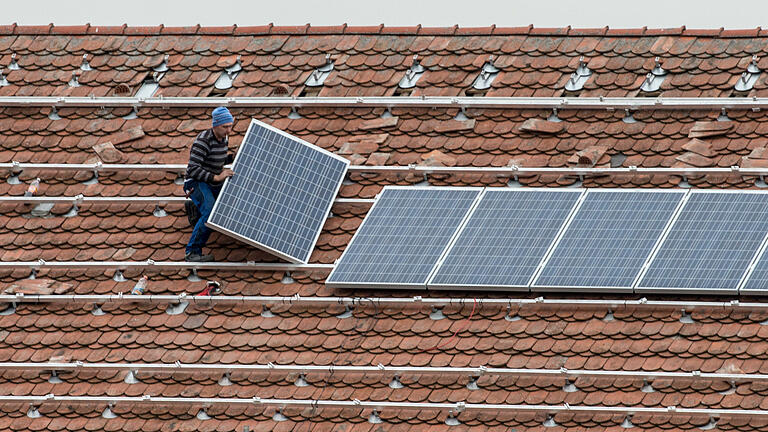 Ein Arbeiter montiert ein Solarmodul auf ein Dach (Archivbild).