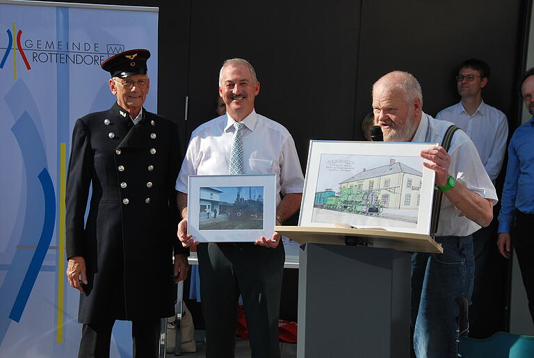 Joachim Kraus (rechts) von den Eisenbahnfreunden Würzburg überreichte Bürgermeister Roland Schmitt (Mitte) eine Originalaufnahme einer Dampflok vor dem Rottendorfer Bahnhof von 1971 und eine von ihm angefertigte Zeichnung des Gebäudes. Joachim Kraus (rechts) von den Eisenbahnfreunden Würzburg überreichte Bürgermeister Roland Schmitt (Mitte) eine Originalaufnahme einer Dampflok vor dem Rottendorfer Bahnhof von 1971 und eine von ihm angefertigte Zeichnung des Gebäudes.