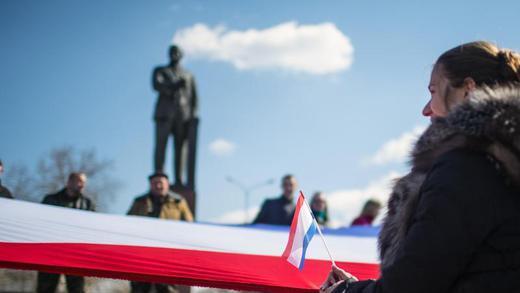 Krise auf der Krim       -  Menschen halten in Simferopol (Ukraine) anlässlich einer Rede von Russlands Präsidenten Putin eine große russische Flagge vor dem Lenin-Denkmal. Foto: Hannibal