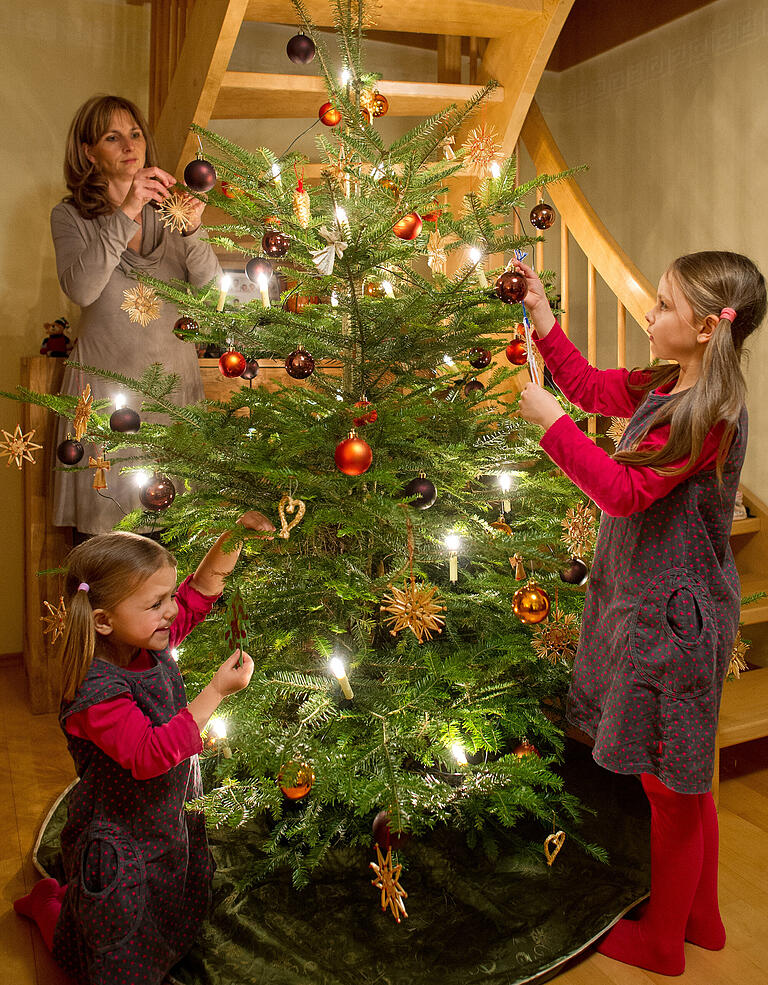 Eine Familie schmückt einen Christbaum (Symbolbild). Eine beliebte Tradition, die in vielen Haushalten nicht fehlen darf.