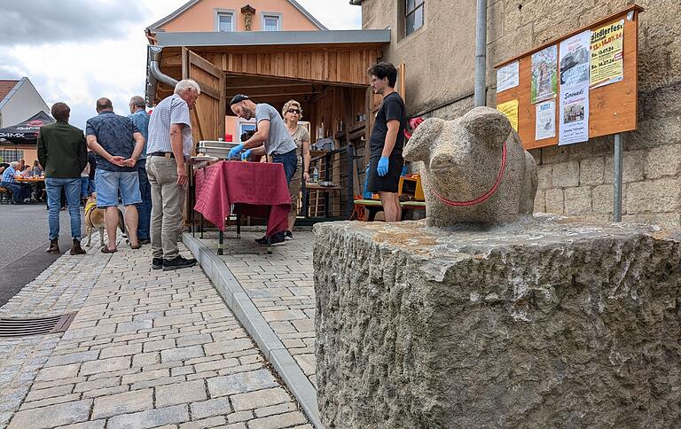 Das gespendete, steinerne Ferkel von Robert Pfeuffer rundet die Aufwertung und Renovierung rund um das Waaghäusle in Hohestadt ab. Im Hintergrund betrachten die Hohestädter Bürgerinnen und Bürger stolz ihr neues Waaghäusle und genießen im Anschluss an den offiziellen Teil ein gemeinsames Mittagessen.