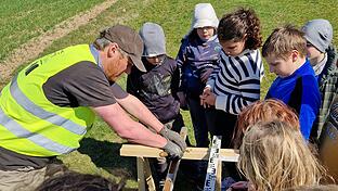 Schülerinnen und Schüler der Grundschule Gräfendorf beobachten einen Archäologen vom Landesamt für Denkmalpflege beim Untersuchen eines Bohrkerns im Lagfeld II.