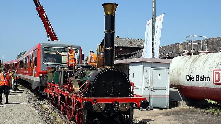 Der Adler ist gelandet       -  Bereits am Samstagmittag kündigte sich das Bahnjubiläum 150 Jahre Tauberbahn im Bahnhof Lauda an.  Um 11.27 Uhr fuhr die E-Lok 111 001-4 vom Eisenbahnmuseum Nürnberg mit einer besonderen Fracht im Bahnhof Lauda ein &ndash; auf Tiefgüterwagen der Nachbau des legendären Adlers von 1835 mit seinem Tender und zwei historischen Personenwagen.  Da auf Gleis 12 kein Strom ist, wurde der wertvolle Fracht mit dem Triebwagen VT 928 553 zur Abladeposition gebracht. Die Zaungäste und Fotografen brauchten jedoch viel Geduld bis das Spektakel schließlich kurz nach 13.30 Uhr begann.  Mit Manneskraft wurden zuerst die Planen entfernt, danach wurde gesichert und kurze Zeit später hing der Tender der Lokomotive am Haken &ndash; nach wenigen Minuten war dieser auf Gleis 12 aufgegleist.  Als nächster war der Adler dran &ndash; auch dieser hing nur wenige Minuten am Schwerlastkranen. Um 13.39 Uhr war der Adler gelandet. Die Eingleisung erfolgte mit viel Schwung und etwas Manneskraft.  Danach kamen die beiden Personenwagen dran. Um 14.15 Uhr trafen schließlich auch die anderen Diesel- und E-Lok-Raritäten im Bahnhof Lauda ein &ndash; alles in einer Zuggarnitur mit zahlreichen historischen Personenwagen &ndash; darunter auch der Rheingold &ndash; gezogen von der historischen E-Lokomotive E 40 128.
