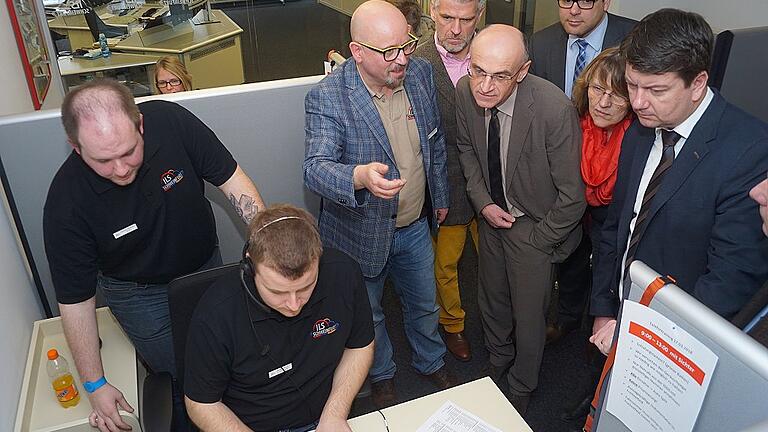 Stresstest für die Integrierte Leitstelle Schweinfurt: Der Disponent Thomas Börmann (links, stehend) schaut Jonas Wehner von der Unterstützungsgrppe - die die Notrufe annimmt - über die Schulter. Rechts erklärt Leitstellenleiter Thomas Schlereth (hellblaues Jacket) den Gästen, was sich gerade dort abspielt.