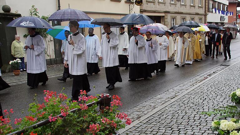 Trotz Regen fand der feierliche Zug zur Kirche statt, vorbei an festlich geschmückten Anwesen mit Fähnchen und Blumenteppichen. Weil die Blaskapelle nicht spielen konnte, stimmten die Priesterseminaristen (im Bild) kurzerhand Lieder an.