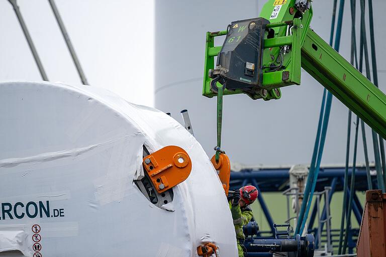 Für den Transport in luftige Höhen montiert ein Bauarbeiter massive Halterungen an einem Windrad-Bauteil. Für den Transport in luftige Höhen montiert ein Bauarbeiter massive Halterungen an einem Windrad-Bauteil.