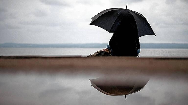 Der Herbst kommt - ARCHIV - Eine Frau sitzt am 19.08.2015 bei verregnetem Wetter unter einem Regenschirm am Ammersee in Herrsching (Bayern). Foto: Matthias Balk/dpa (zu dpa 'Der Herbst kommt: die schönen und die tristen Seiten' vom 31.08.2015) +++(c) dpa - Bildfunk+++ Der Herbst kommt - ARCHIV - Eine Frau sitzt am 19.08.2015 bei verregnetem Wetter unter einem Regenschirm am Ammersee in Herrsching (Bayern). Foto: Matthias Balk/dpa (zu dpa 'Der Herbst kommt: die schönen und die tristen Seiten' vom 31.08.2015) +++(c) dpa - Bildfunk+++
