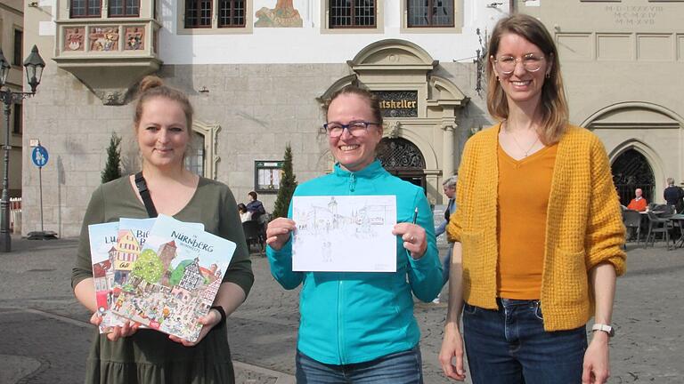 Die Verlegerinnen des Velle Verlages, Deborah Schulze (links) und Tabea Lerch (rechts) sowie die Illustratorin Brigitte Kuka präsentieren die Motive des Rathaus-Motivs.