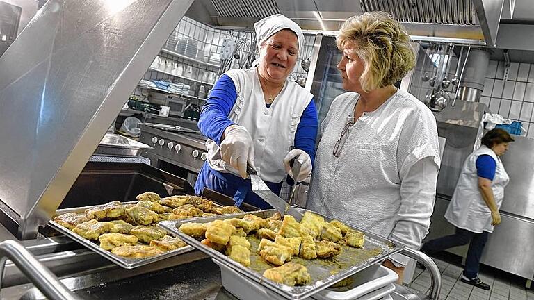 Schulessen       -  Fisch auf den Tisch: Küchen-Mitarbeiterin Kalthoum Sakgi (links) legt in der Küche des Droste-Hülshoff-Gymnasiums in Meesburg (Baden-Württemberg) Seelachs-Filets in eine Kippbratpfanne, während Köchin Alexandra Nied daneben steht und sich mit ihr abspricht.