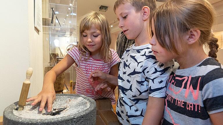 Die Nachbildung einer Handmühle der römischen Legionäre fasziniert Kinder im Malerwinkelhaus immer wieder. Hier sind es Maya, Johannes (beide 7) und Emma (6) während einer Ferienpassaktion.