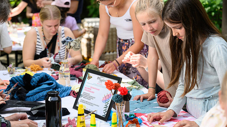 Fair liebt Kunst Festival - Kreativ- und Designmarkt       -  Ein paar Kinder basteln am Sonntag (21.05.23) beim Kreativ- und Designmarkt unterhalb des Zeller Tors in Würzburg in einem Workshop bunte Wimpelketten. Der Markt ist Teil des Fair liebt Kunst Festivals, das am Wochenende an verschiedenen Locations in der Zellerau stattfindet. Junge Künstlerinnen und Designer bieten ihre Werke an, bei verschiedenen Workshops können die Besucherinnen und Besucher selber aktiv werden.