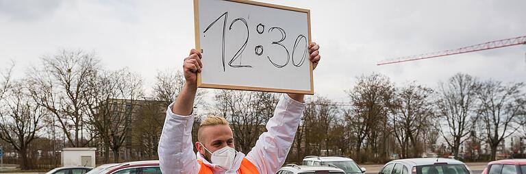 Mitarbeiter des Impfzentrums zeigen mit Plakaten, welches Termin-Zeitfenster aktuell ist, das heißt, wer an den Eingang kommen soll. Mitarbeiter des Impfzentrums zeigen mit Plakaten, welches Termin-Zeitfenster aktuell ist, das heißt, wer an den Eingang kommen soll. 