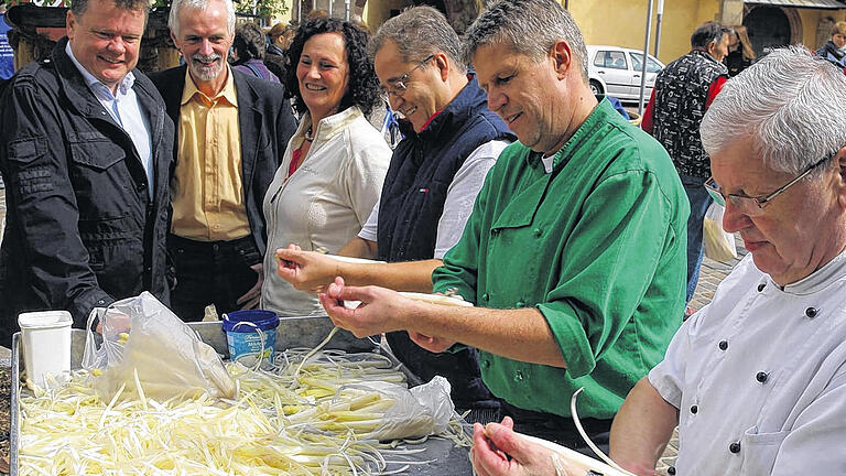 300 Kilogramm Spargel geschält       -  (ka)   Wie schon 2011 wurde auch bei der diesjährigen Spargelschälaktion die Rekordmarke von insgesamt 300 Kilogramm verkauftem Spargel erreicht. Den Großteil davon schälten die Karlstadter Wirte und ihre Köche gegen eine freiwillige Spende zugunsten der Musikschule küchenfertig. Diese sorgte mit Standkonzerten des Blechbläserensembles, der Jazz-Combo, des Percussion-Ensembles und von Saxofun für musikalische Unterhaltung. Auch Spargelcremesuppe und fränkischer Schoppen wurden bei der Aktion  auf dem Kübelmarkt angeboten. Der Spargel wurde von der Familie Schnackig aus Schönarts und dem Obst- und Gemüsebauern Gold aus Karlburg geliefert. Im Bild staunen (von links) Dietholf Schröder, Geschäftsführer der Stadtmarketing GmbH, Alexander Streib, Leiter der Musikschule und die stellvertretende Bürgermeisterin Anni Kühl-Johannes über die Fingerfertigkeit von Michael Schulze (Bistro Chez Michel), Udo Vollert (Zum Fehmelbauern) und Heinz Reimer (Reimers Stuben).