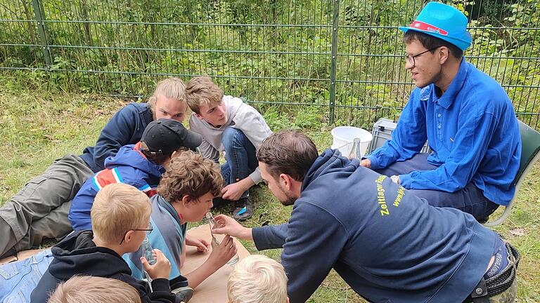 Paul-Philip Gläser (sitzend) stellte beim Lagerspiel an der Station „Luft und Wasser“ der Gruppe „Jungs 1“, mit ihren Zeltbetreuern Ulrich Schnös (links liegend) und Lukas Vogel (rechts kniend), die Aufgabe ein Lied auf der Wasserflaschenpanflöte zu spielen.