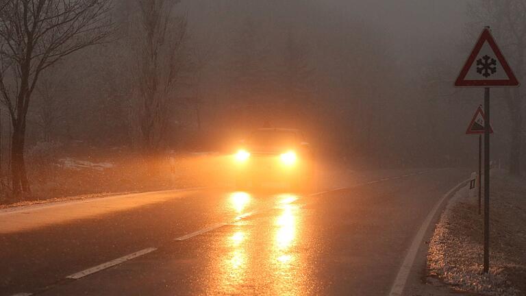 Glätte       -  Ein Auto fährt bei Glatteis und Nebel über eine Straße. (Symbolbild)